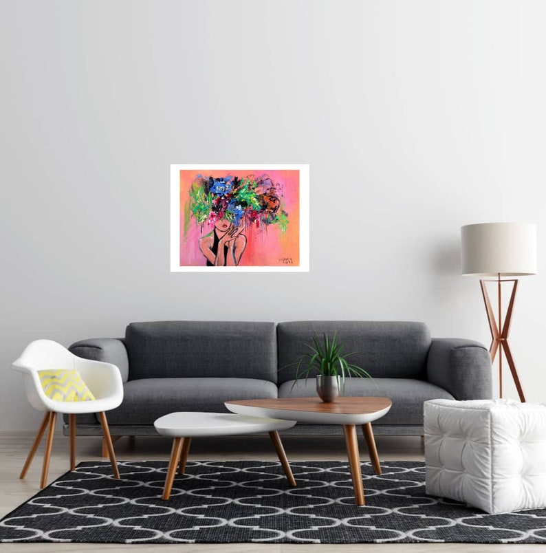 May include: An abstract art print featuring a woman with a floral headpiece. The artwork has a pink and orange background with a white border. The woman's face is partially visible, with red lips. The floral headpiece is a mix of blue, green, and purple.