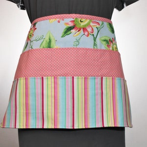 May include: A pink and blue striped apron with a floral print top and a polka dot middle section.