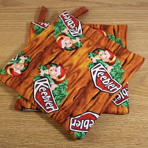 May include: Set of three brown and orange fabric pot holders with a woodgrain pattern. The pot holders feature a repeated image of a Keebler elf and the Keebler logo.
