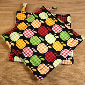 May include: Two black pot holders with a pattern of red, green, yellow, and white gingham apples. The pot holders have a loop for hanging.
