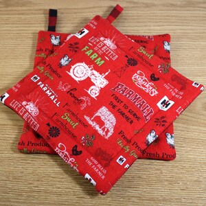 May include: Two red quilted pot holders with a farmhouse theme. The pot holders feature a white tractor, a cow, chickens, and the text "Life is better on the farm" and "Farmall First to Serve the Farmer".