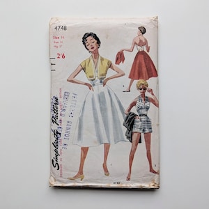 Puede incluir: Sobre de patrón Simplicity vintage con ilustraciones de diseños de ropa de mujer. Los diseños incluyen un vestido, un conjunto de top y shorts halter y un conjunto de falda y bolero. El sobre está envejecido con texto y números.