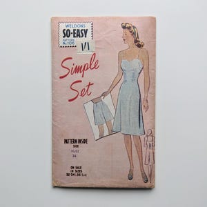 Puede incluir: Patrón de costura vintage titulado "Weldons So-Easy Simple Set". La portada presenta una mujer con un vestido azul claro, sosteniendo un dibujo de pantalones cortos. El patrón es para una talla de busto 34 y está disponible en tallas 32, 34 y 36.