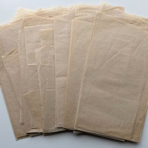 Puede incluir: Una pila de hojas rectangulares de papel pergamino de color marr&oacute;n claro. El papel tiene una calidad ligeramente transl&uacute;cida y una textura arrugada. Las hojas est&aacute;n dispuestas en forma de abanico, con los bordes visibles.