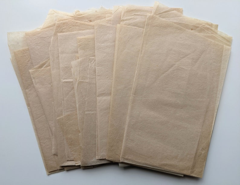 Puede incluir: Una pila de hojas rectangulares de papel pergamino de color marr&oacute;n claro. El papel tiene una calidad ligeramente transl&uacute;cida y una textura arrugada. Las hojas est&aacute;n dispuestas en forma de abanico, con los bordes visibles.