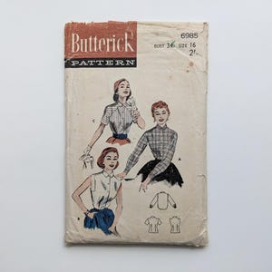 Könnte beinhalten: Vintage Butterick Schnittmusterumschlag. Der Umschlag ist beige mit Illustrationen von Frauen, die Blusen tragen. Die Oberseite des Umschlags ist dunkelbraun mit dem Butterick-Logo. Die Schnittmusternummer ist 6985, Größe 16, Brustumfang 86 cm.
