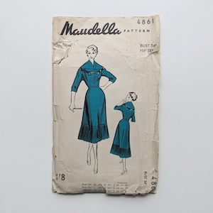 May include: Vintage Maudella sewing pattern featuring illustrations of a teal dress with a pleated skirt and a matching shorter version. The pattern is printed on aged paper with the text "Maudella PATTERN" at the top, along with size information.