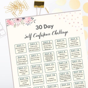May include: A cream-coloured 30-Day Self Confidence Challenge printable with floral accents. The challenge includes daily prompts for self-reflection and personal growth. Gold paper clips and a keyboard are in the background.