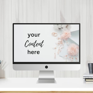 以下が含まれることがあります： 画面が白く、銀色のデスクトップパソコン。背景にはピンクの花、綿、金色の指輪が飾られています。画面には「your content here」というテキストが表示されています。