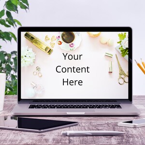 May include: A laptop computer with a blank screen displaying the text "Your Content Here" on a pink background with decorative items, such as a cup of coffee, flowers, and stationery. The laptop is on a wooden table with a tablet, a pen, and a cell phone.