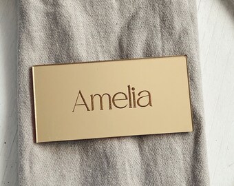 May include: Gold place card with the name Amelia engraved on it.