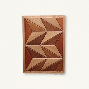 May include: A rectangular wooden wall art piece featuring a geometric pattern of interlocking triangles in varying shades of light and dark brown wood grain. The artwork is enclosed in a simple wooden frame and includes the text CAST & WOOD.