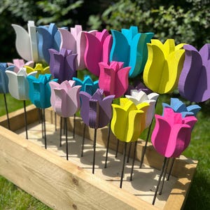 May include: A wooden planter box filled with colourful wooden tulip flower decorations. The tulips are painted in various shades of pink, purple, blue, yellow, and white. The planter box is made of natural wood and has a rustic look.