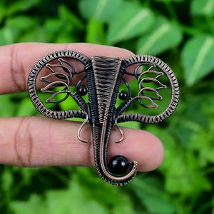 May include: A wire-wrapped elephant pendant with black beads for eyes and a black bead at the bottom of the trunk. The pendant is made of copper wire and is a dark bronze color.