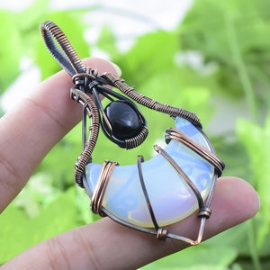 May include: A crescent moon shaped opal pendant wrapped in copper wire with a black gemstone accent.