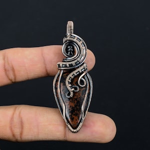 May include: A copper wire wrapped pendant featuring a brown and black speckled stone. The pendant is shaped like a teardrop and has a wire loop at the top for hanging.