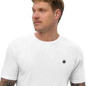 May include: White short-sleeved t-shirt with a small, round, embroidered design on the left chest.