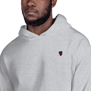 May include: A heather gray hooded sweatshirt with a small embroidered design on the left chest. The design is a black and red stylized heart.
