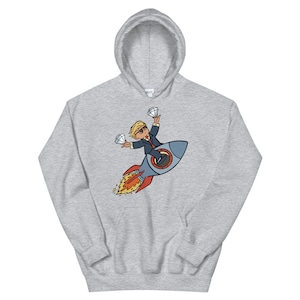 Könnte beinhalten: Ein hellgrauer Kapuzenpullover mit einer Cartoon-Illustration einer Person im Anzug, die auf einer Rakete reitet und zwei Diamanten hält. Die Rakete hat rote und blaue Akzente mit Flammen. Der Kapuzenpullover hat eine Kapuze mit Kordelzug.