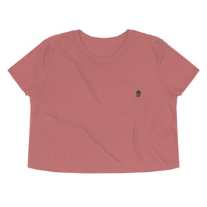 May include: A cropped, short-sleeved t-shirt in a dusty rose color with a small embroidered design on the left chest.