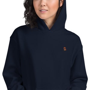 May include: A navy blue hooded sweatshirt with a small embroidered image of a person wearing sunglasses.