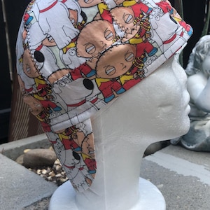 Peut inclure: Casquette de soudeur blanche ornée d'un motif répété de personnages de dessins animés aux couleurs vives. La casquette est dotée d'un rabat pour protéger le cou et les oreilles. Le motif comprend des personnages.