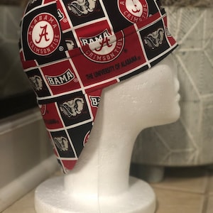 May include: A red and black patterned welding cap with the University of Alabama logo and the words "Bama", "Crimson Tide", and "The University of Alabama".