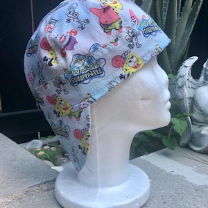 Puede incluir: Gorra de soldadura azul claro con un patrón repetido de personajes de Bob Esponja. La gorra tiene una visera y una corona redondeada. Las palabras "SpongeBob SquarePants" están impresas en la gorra. La gorra se muestra en una cabeza de maniquí blanca.