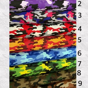 May include: A stack of ten rolls of camouflage fabric in various colors. The colors include pink, purple, blue, green, brown, and red. Each roll displays a unique camouflage pattern, suitable for apparel or crafting projects.