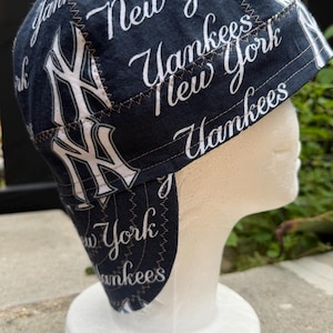 Op de afbeelding: Een donker marineblauwe laskap met een herhalende witte print van het New York Yankees logo en de tekst New York Yankees. De kap is geconstrueerd met meerdere stoffen panelen die zijn verbonden door zichtbare bruine zigzagstiksels.