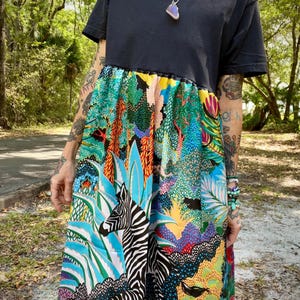 May include: A black t-shirt with a colorful, patterned skirt featuring a zebra, plants, and flowers. The skirt is attached to the t-shirt, creating a unique dress.