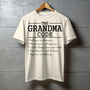 May include: A cream-colored short-sleeve t-shirt featuring the black text THE GRANDMA CODE followed by a numbered list: 5. Bedtime is whenever, 4. The answer is always yes, 3. I will always have your back, 2. Mom doesn't need to know, 1. Hugs are mandatory.