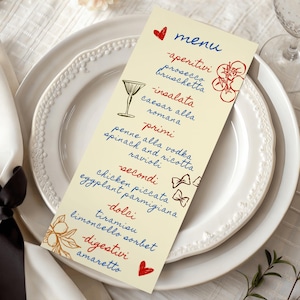 May include: A cream-colored menu card with handwritten text in blue and red, featuring Italian food categories and dishes. Decorative illustrations include a cocktail glass, tomatoes, and bows. The menu rests on a white plate with a decorative rim.