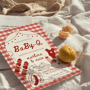 Op de afbeelding: Een uitnodiging voor een babyshower met een rood-wit geruit patroon. De uitnodiging luidt "Baby-Q" en bevat illustraties met barbecue-thema. Een hele citroen en gepelde sinaasappelsegmenten zijn ook zichtbaar.