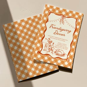 May include: Two rectangular cards with an orange and white gingham pattern. The top card features a decorative border and text reading Friendsgiving Dinner, Join us for a thanksgiving dinner party, bring your best dish to share, Sunday 4:00 PM, November 15, 2025, in Aspen Drive, New Jersey, RSVP to Cam at 456-7890, with illustrations of a turkey, wine, and candles.