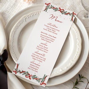 May include: A vertical white menu card featuring red script text and a festive border of green pine branches and red ribbons. The menu lists starters, main course, sides, desserts, and drinks, including items like Creamy Pumpkin Soup and Roasted Herb Turkey.