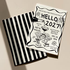以下が含まれることがあります： シャンパンボトルからクープグラスに注ぐ様子や花火、Hello 2027の文字が黒いインクで描かれた白い大晦日のパーティー招待状と、黒い縦縞模様が施されたお揃いの封筒のセット。