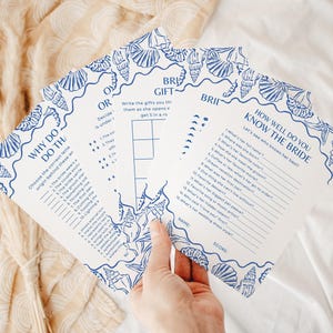 May include: A set of white bridal shower game cards featuring a blue seashell border pattern. The cards include titles such as How Well Do You Know The Bride, Gift Bingo, and Why Do That, with printed questions, blank lines for answers, and score sections.