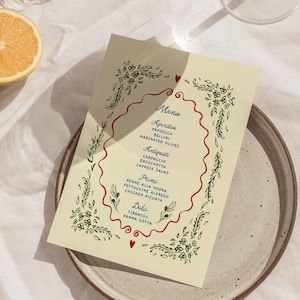 Peut inclure: Une carte de menu rectangulaire de couleur crème avec une bordure festonnée rouge centrale et des illustrations florales vertes dans les coins. Le texte liste les sections Menu, Aperitivi, Antipasti, Primi et Dolci avec divers plats.