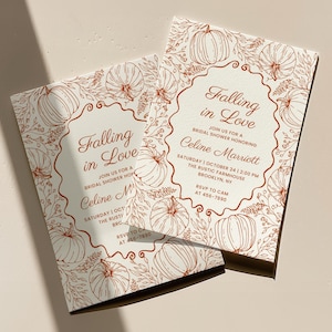 May include: Two white bridal shower invitation cards with rust-coloured line art featuring pumpkins and foliage. The text reads: Falling in Love, join us for a bridal shower honouring Celine Marriott, Saturday, October 24, 2:00 PM, The Rustic Farmhouse, Brooklyn, NY, RSVP to Cam at 456-7890.