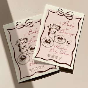 Peut inclure: Deux cartons d'invitation roses pour une baby shower avec des illustrations marron de cafetières, de tasses et le texte "a Baby is Brewing". Les invitations incluent le texte "Kayla's Baby Shower" et les détails de l'événement.