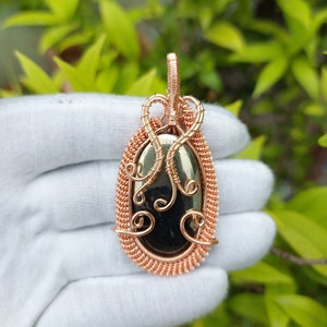 May include: A copper wire wrapped pendant featuring a black oval gemstone. The pendant has a delicate, intricate design with swirls and loops.
