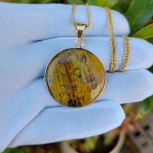 Könnte beinhalten: Eine goldene Kettenkette mit einem runden Anhänger aus Tigerauge. Der Anhänger ist tief goldgelb mit braunen und schwarzen Streifen.