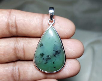 May include: A teardrop-shaped pendant with a light green stone and a silver-colored metal frame. The stone has dark green and black inclusions. The pendant has a silver bail for a chain.