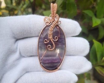 May include: A purple and white fluorite gemstone pendant wrapped in copper wire. The wire is twisted into a decorative design.
