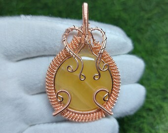 May include: A copper wire wrapped pendant featuring a yellow agate stone. The pendant has a delicate, intricate design with swirls and loops.
