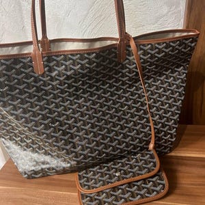 May include: A large tote bag and matching wallet set. The bags feature a repeating geometric pattern in brown, black, and white. The trim and handles are a light brown color. The wallet has a snap closure and a small strap.