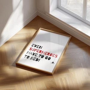 May include: A framed print with the text "EVEN SUPERHEROES HAVE TO GO TO BED!" in black and red lettering. A small black spider graphic is below the text.