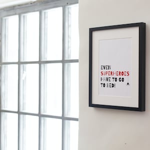 May include: A black framed print with a white background and red text that reads "Even superheroes have to go to bed!" with a small black spider graphic at the bottom.