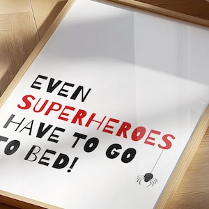 May include: A framed print with the text "Even superheroes have to go to bed!" in black and red lettering. A black spider with a red body hangs from a string above the text.